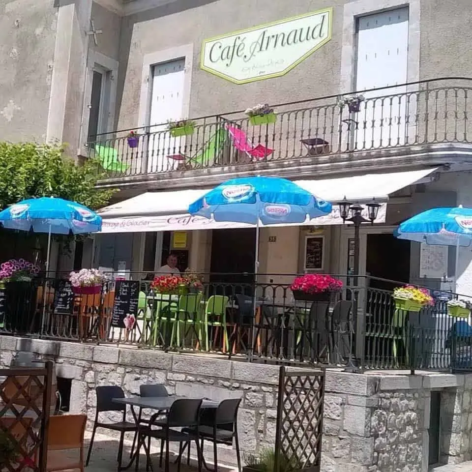 Façade du Café Arnaud avec les balcons fleuris des chambres au-dessus de la terrasse