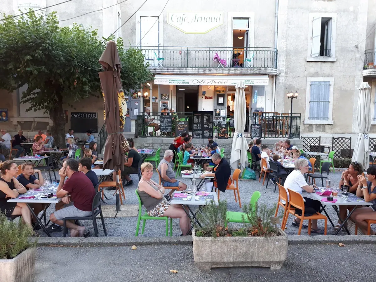 La terrasse du Café Arnaud remplie de clients devant la façade, un soir d'été à Ruoms