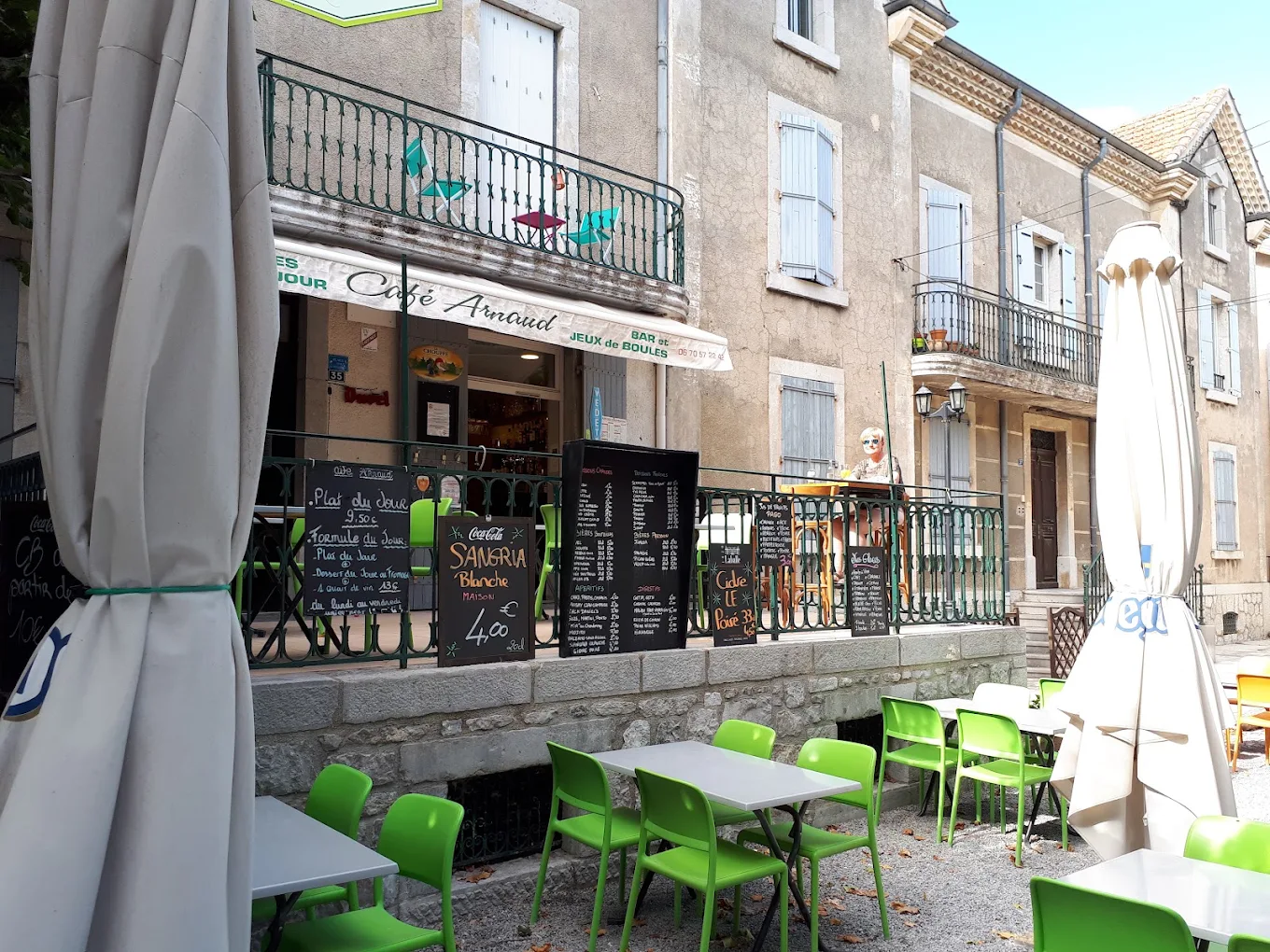 Terrasse du Café Arnaud à Ruoms avec ses chaises vertes et les ardoises du jour